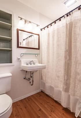 A cream bathroom with ceramic sink and toilet, built in shelving and a towel rack.