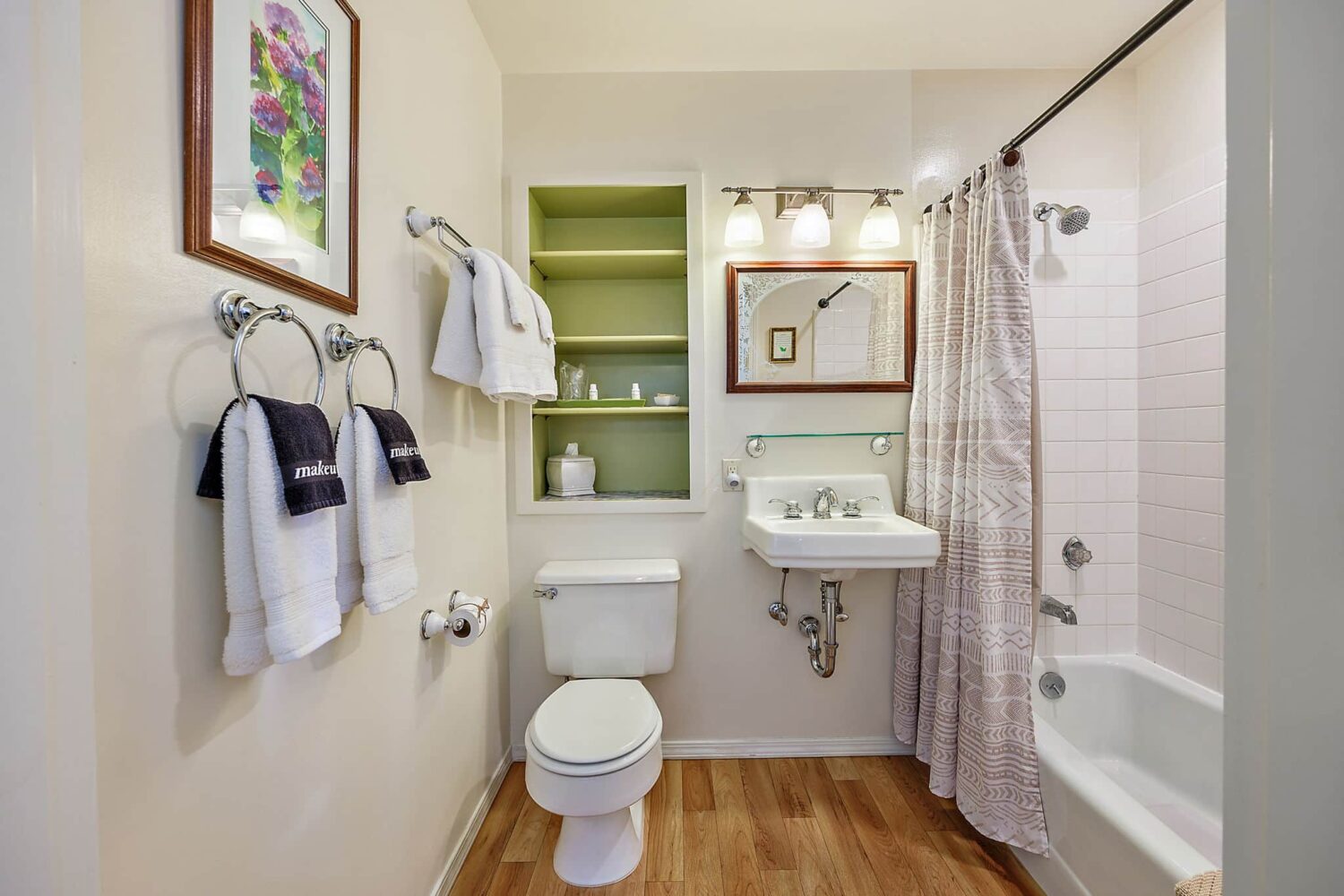 A cream bathroom with ceramic sink and toilet, built in shelving and a towel rack.