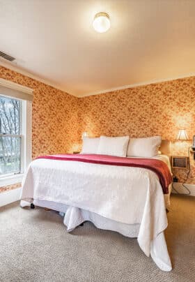 Maroon and White floral wallpapered guest room with maroon and white bedding and carpeted flooring