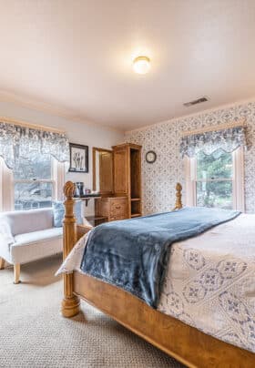 Guest room with blue and white bedding, wooden bed frame, and blue and white printed wallpaper