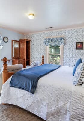 Guest room with blue and white bedding, wooden bed frame, and blue and white printed wallpaper