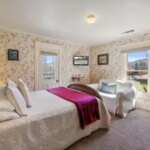 Wallpapered guest room with maroon and white bedding, a wooden closet with a mirror, and a doorway to the bathroom