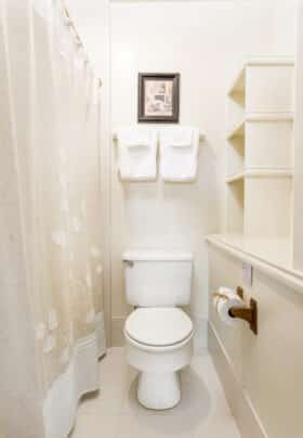 Cream bathroom with built in shelving, ceramic appliances and a white alcove bathtub with a tan shower curtain