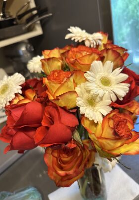 A bouquet of vibrant pink and yellow roses with a few green leaves poking through